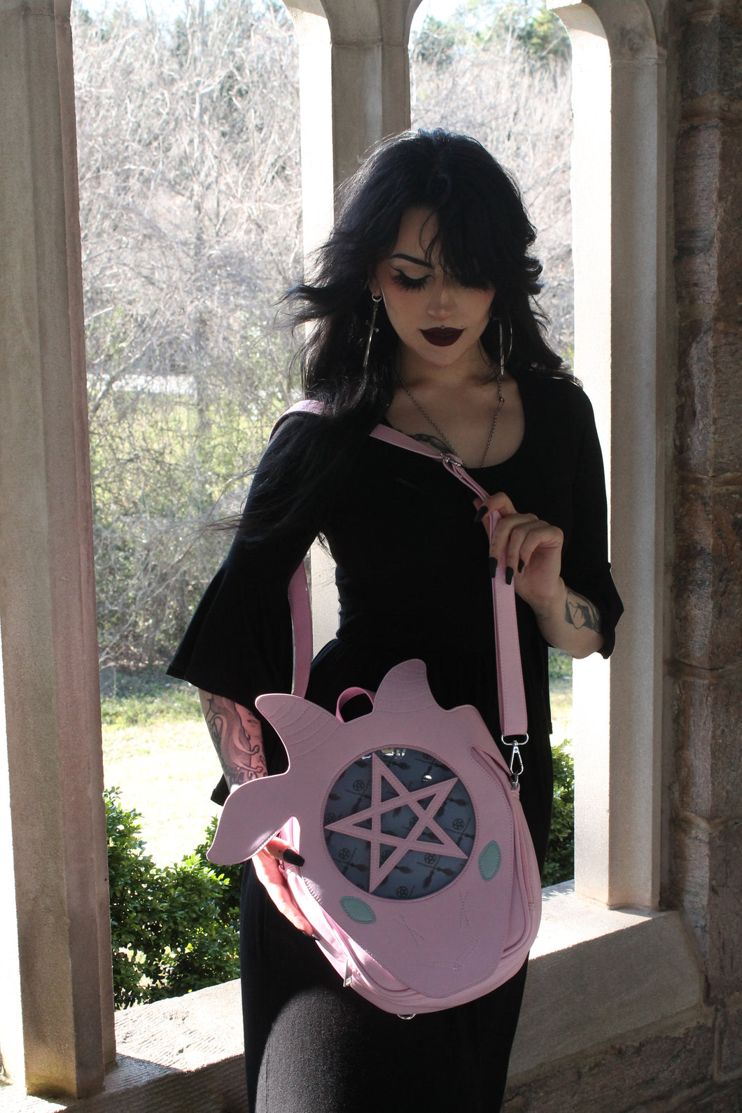 Person holding a pink bag with a pentagram design outdoors.